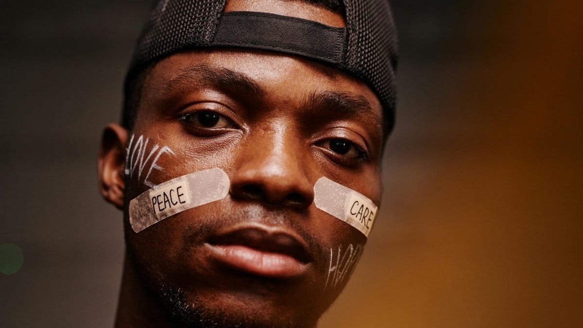 Close-up portrait of a man with band aids displaying 'peace' and 'care' messages.