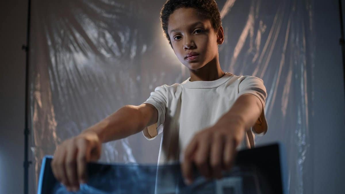 A young boy with short hair holds an X-ray, standing in a studio with plastic foil backdrop.