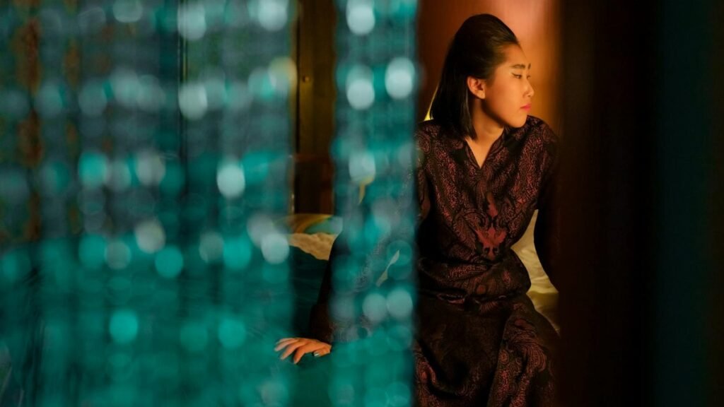 Asian woman sitting thoughtfully behind a beaded curtain, creating a serene indoor ambiance.