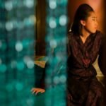 Asian woman sitting thoughtfully behind a beaded curtain, creating a serene indoor ambiance.