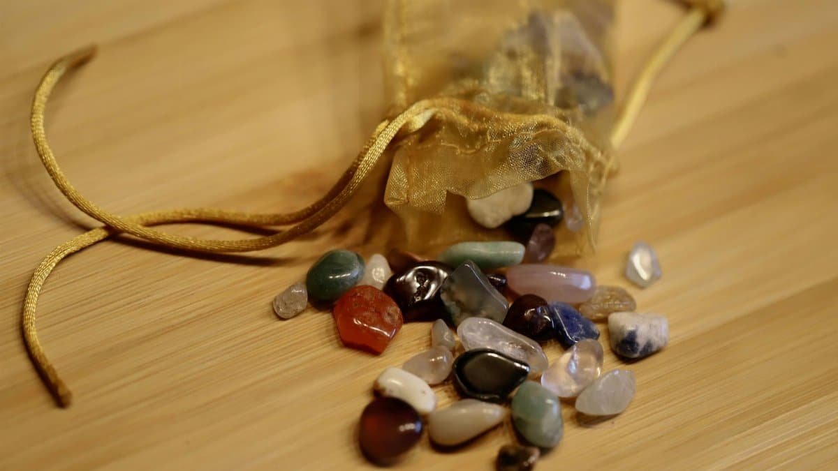 A collection of colorful healing stones spilling from a golden pouch on a wooden surface.