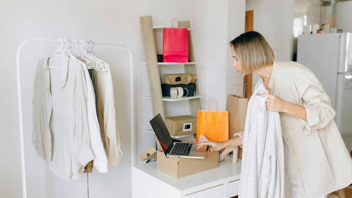 A woman in casual attire unpacking a delivery box with clothing at home, engaging in online shopping.