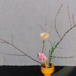 A serene minimalist floral arrangement in a wooden vase with branches and blooms.