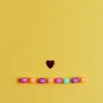 Bright minimalist arrangement with a heart and 'YOURSELF' on yellow background.