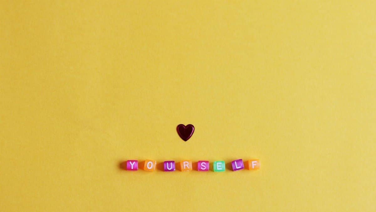 Bright minimalist arrangement with a heart and 'YOURSELF' on yellow background.