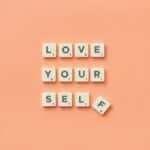Scrabble tiles spelling 'Love Yourself' on a peach background, inspiring self-care.