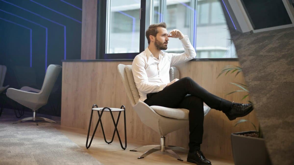 A thoughtful man in a modern office interior, sitting and looking outside.