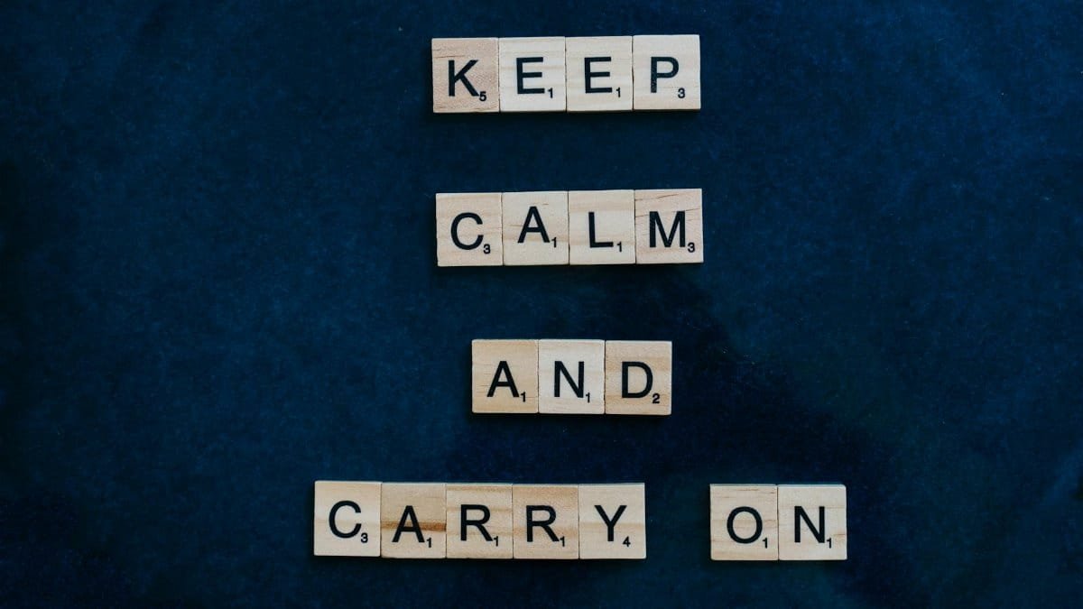 Wooden Scrabble tiles spelling 'Keep Calm and Carry On' on a dark background, promoting positivity.