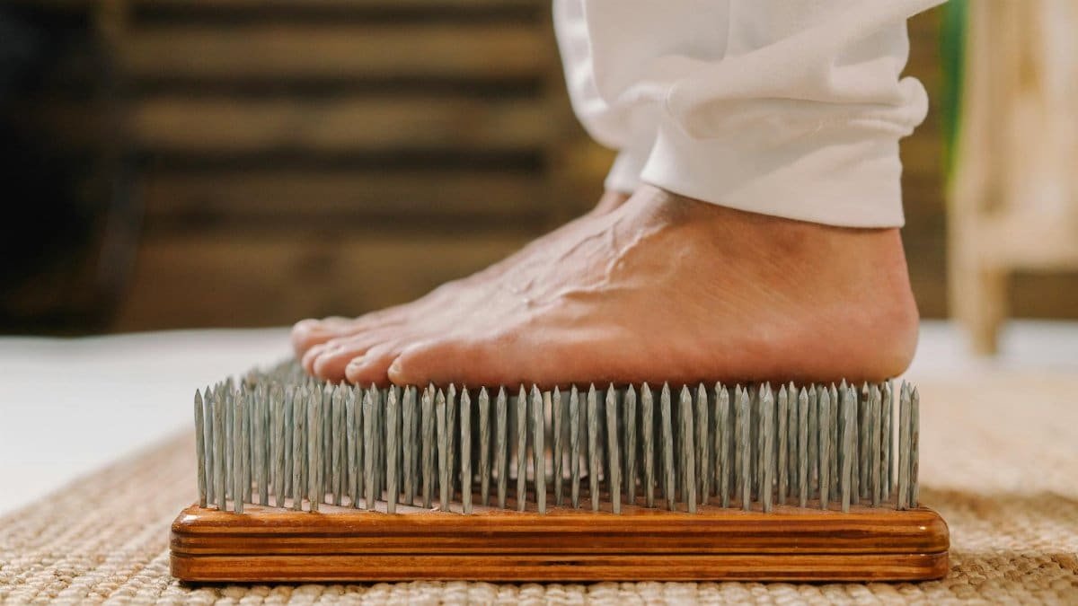 A close-up shot of a barefoot person standing on a nail board, used in meditation and pain tolerance practices.