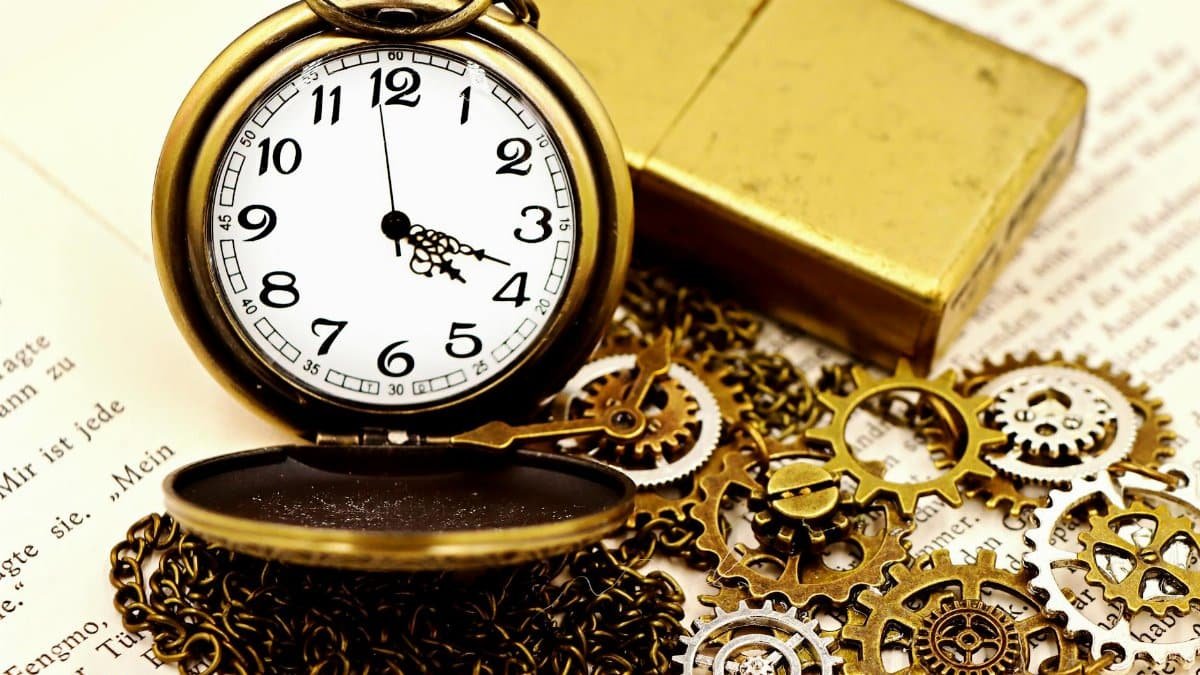 Close-up of an antique pocket watch with gears, chain, and gold lighter on open book pages.