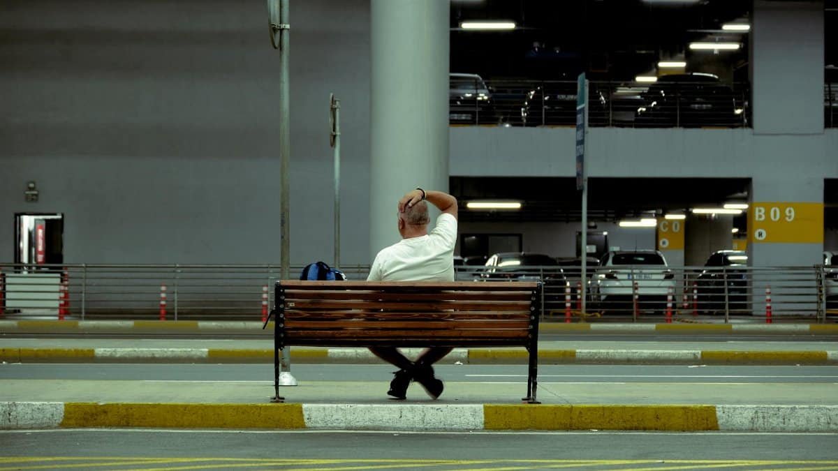 A man sitting alone on a bench in a parking area, urban solitude.