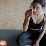 A woman practicing meditation on a yoga mat, focusing with eyes closed next to a candle indoors.