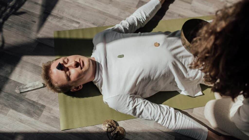 Man lying on yoga mat with healing crystals during meditation for relaxation and balance.