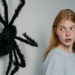 A woman shows fear as she encounters a large wall-mounted spider, highlighting themes of anxiety.