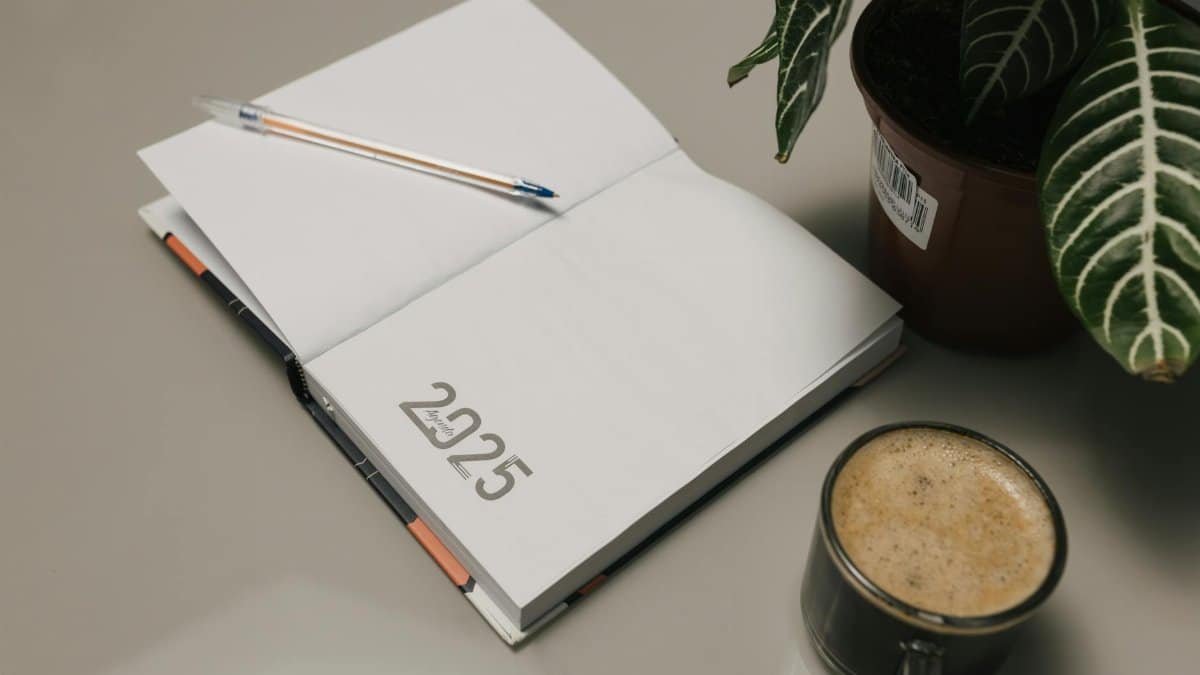 Open 2025 planner with a pen, coffee, and potted plant on a desk.