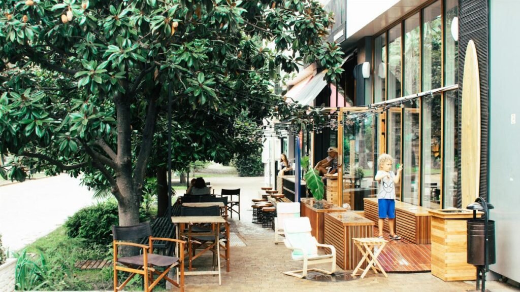 Bright outdoor café featuring families, lush greenery, and children playing in daylight.