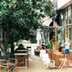Bright outdoor café featuring families, lush greenery, and children playing in daylight.