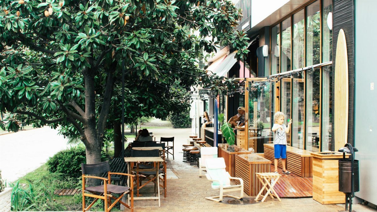 Bright outdoor café featuring families, lush greenery, and children playing in daylight.