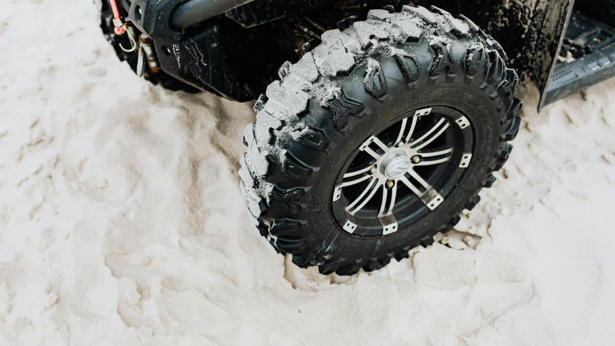 Close-up of an off-road vehicle tire on sandy beach terrain, showcasing rugged tread design.
