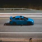 A sleek blue car driving on an empty highway at night, exuding speed and freedom.