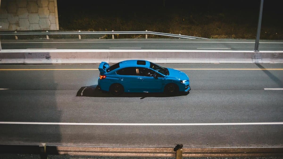 A sleek blue car driving on an empty highway at night, exuding speed and freedom.
