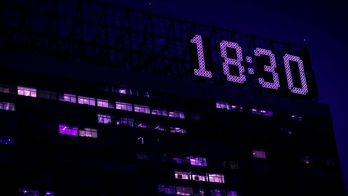 A modern building is illuminated at night with a prominent digital clock showing 18:30.