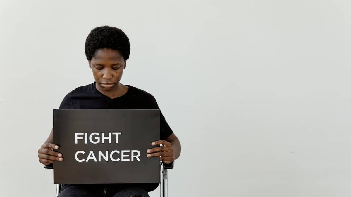 A woman holds a sign that reads 'Fight Cancer' in a studio setting with a minimalist look.