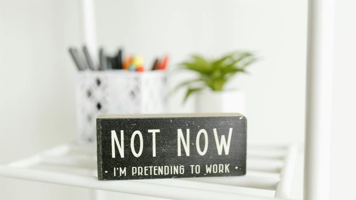 Close-up of a funny desk sign reading 'Not now, I'm pretending to work' in a modern office.