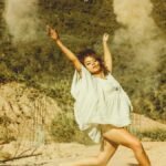 Young woman energetically dancing in an outdoor dusty setting with arms raised.