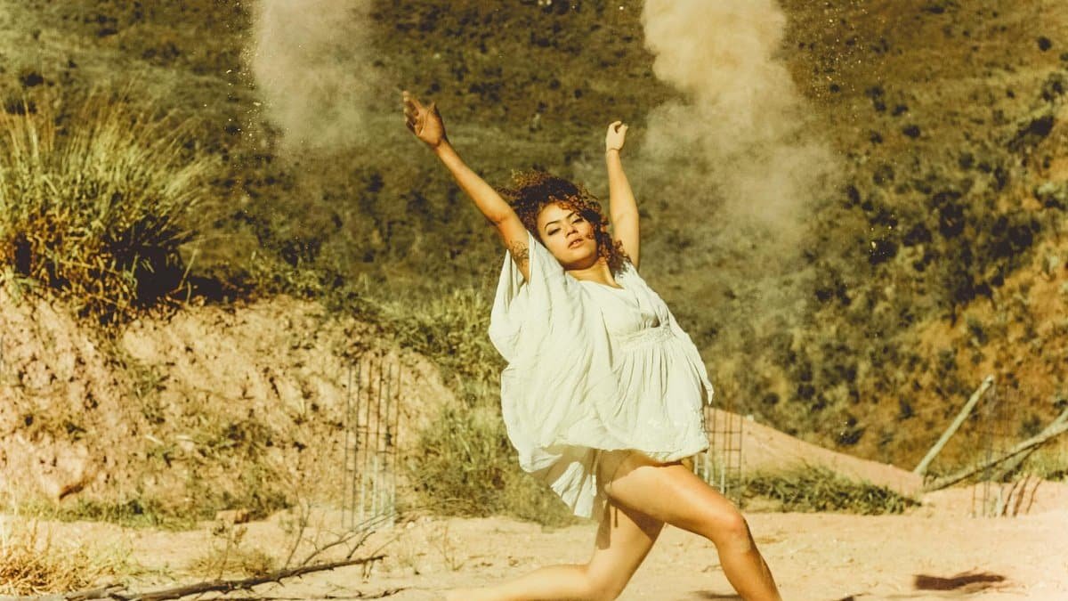 Young woman energetically dancing in an outdoor dusty setting with arms raised.