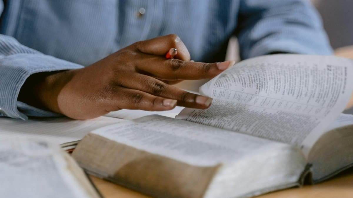 A person wearing a blue shirt flipping through a Bible, highlighting faith and study.