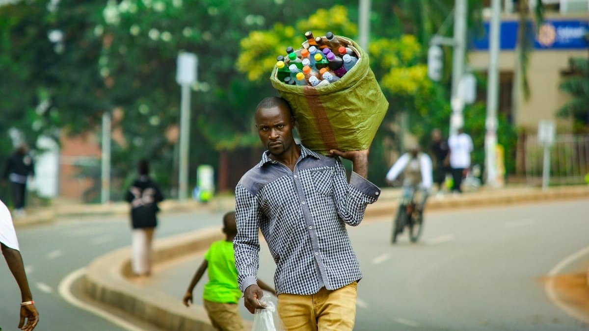 Man carrying a bundle of bottles in Kampala, Uganda, showcasing vibrant street life.