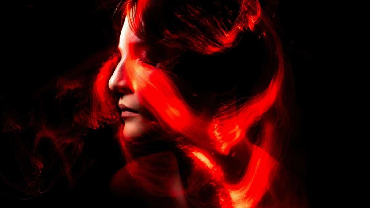 Artistic portrait featuring red light trails swirling around a woman's face against a dark background.