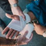 Close-up of two people bandaging an injured hand outdoors, focusing on first aid care.