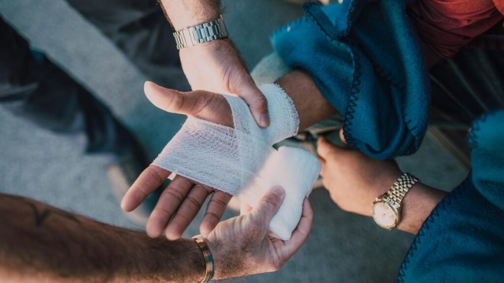 Close-up of two people bandaging an injured hand outdoors, focusing on first aid care.