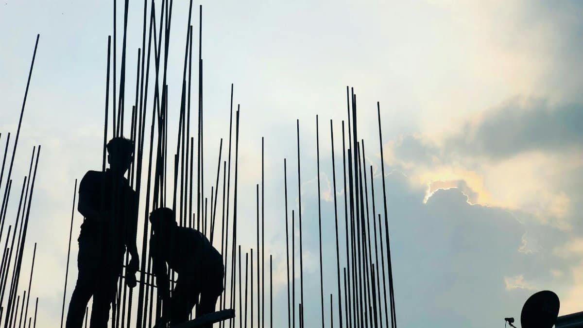 Silhouetted construction workers on site at dawn in Dhaka, Bangladesh, against a cloudy sky.