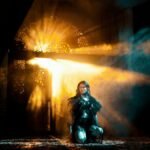 A young woman kneels in dramatic light and shadows, creating an ethereal atmosphere.