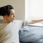 Young ethnic male adolescent taking mobile phone from windowsill after awakening in morning in bedroom