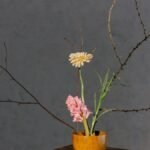 A minimalist floral arrangement in a wooden vase with branches and soft lighting.