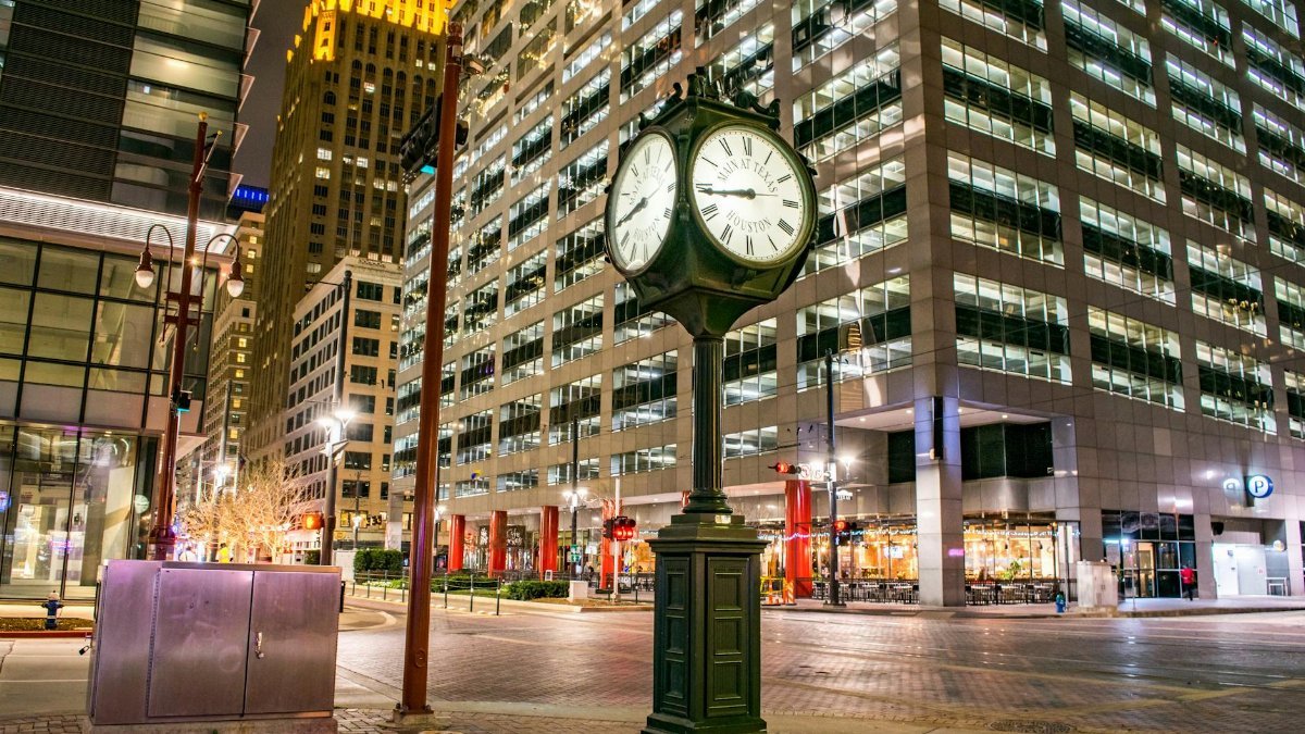 Illuminated clock and modern skyscrapers in downtown Houston at night.