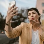 Woman in a casual outfit taking a selfie on a sunny city street.