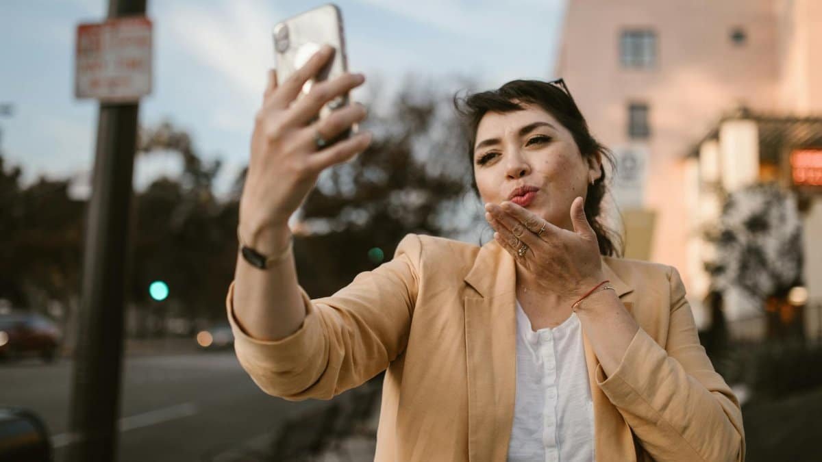 Woman in a casual outfit taking a selfie on a sunny city street.