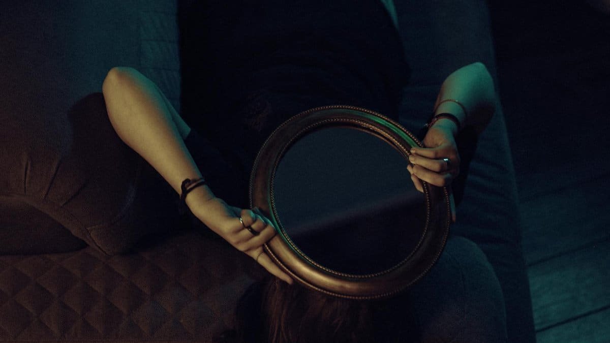 An enigmatic scene of a woman lying on a couch holding a mirror, creating a sense of intrigue.