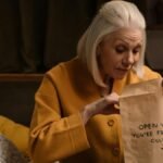 Senior woman in yellow unpacking a mysterious gift in a cozy bedroom setting.