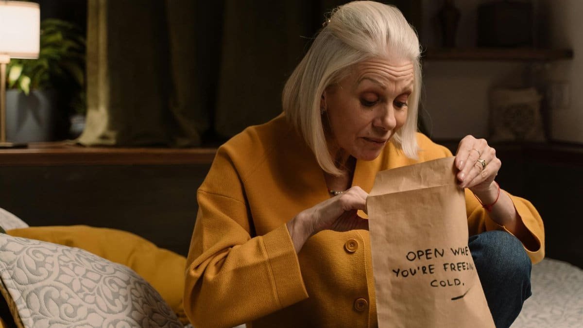Senior woman in yellow unpacking a mysterious gift in a cozy bedroom setting.