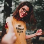 Cheerful woman in glasses holding hands outdoors, wearing a text t-shirt.