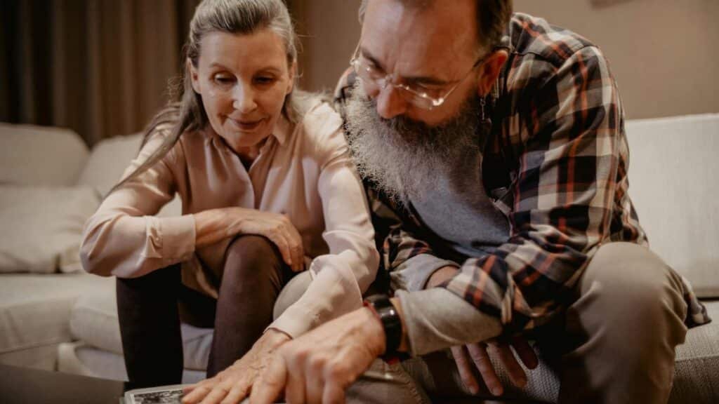 An elderly couple enjoys looking at an album, reminiscing about happy past moments.