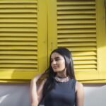 Elegant woman posing in front of yellow shutters, showcasing modern fashion.