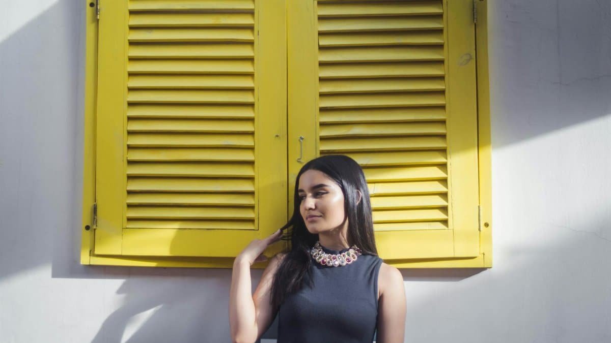 Elegant woman posing in front of yellow shutters, showcasing modern fashion.