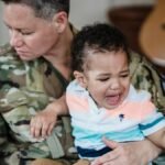 A soldier in uniform comforts a crying child, depicting the emotional bond and sacrifice of military families.